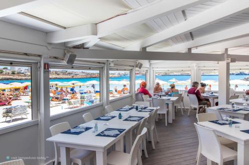 兰佩杜萨吉提亚汤马西诺酒店的一间设有白色桌椅的餐厅以及海滩