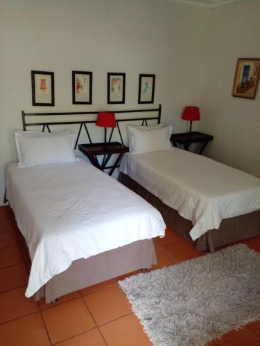 赫卢赫卢韦HLULALA GUEST HOUSE的客房内的两张床,配有白色床单和红色灯。