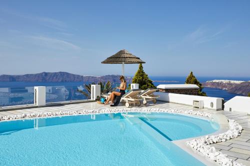 易莫洛林Santorini Princess Spa Hotel的坐在游泳池旁的伞下的女人