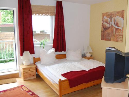 奥门豪斯特Ferienwohnungen Haus Mecklenburg的一间卧室配有一张带红色窗帘的床和电视。