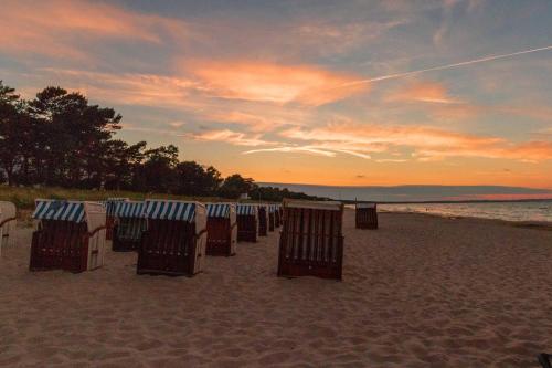 宾茨Ferienwohnung Meeresbrise的日落时在海滩上摆放一排沙滩椅