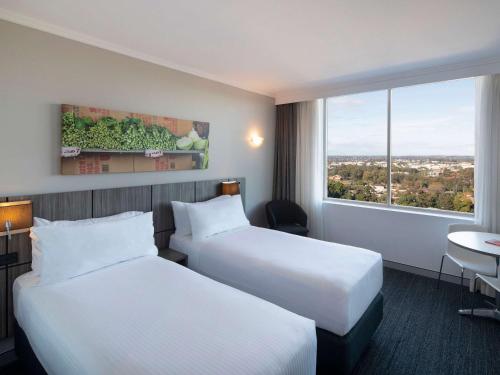 班克斯镇Mercure Sydney Bankstown的酒店客房设有两张床和窗户。