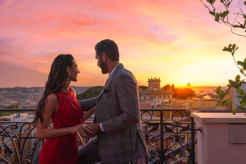 罗马巴廖尼女王饭店 –立鼎世酒店集团的男人和女人站在一个享有日落美景的阳台上