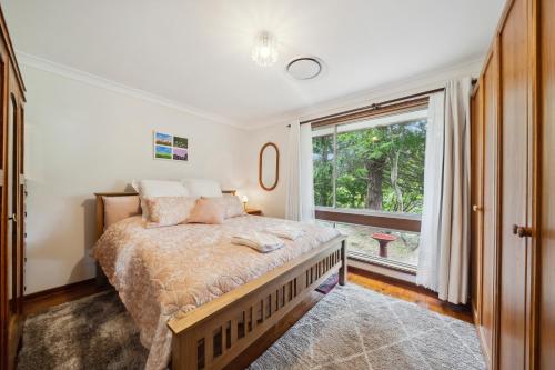 卢拉Azalea Cottage, Leura NSW Australia的一间卧室设有一张床和一个大窗户