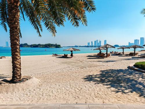 迪拜Seaside Serenity Residence Elegant 1BR Escape in Palm Jumeirah by La Buena vida holiday homes的沙滩上,有遮阳伞,有人坐在沙滩上