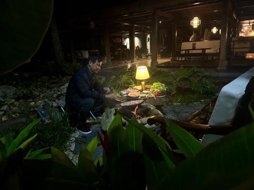 河江Thavill Retreat HaGiang的坐在花园里的男人,晚上拿着灯