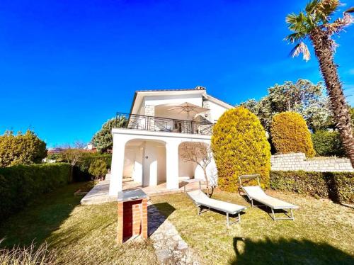 努马纳Villa Edith - stupenda villa con terrazzo vista mare, giardino e spiaggia inclusa的一座房子,配有两把椅子和一棵棕榈树