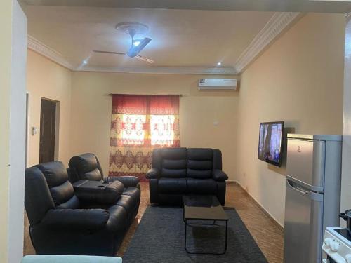 BrikamaIzzy Guest House的客厅配有黑色皮革家具和电视