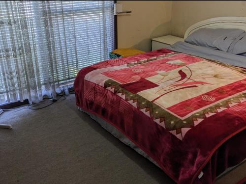 悉尼#BIDWILL GARDENS ON MIDDLETON# Private Room King Size Bed OR Open Lounge Room Floor Mattress SHARED Bathroom FREE Kitchen Essentials Fast NBN WIFI HDTV KAYO Sports Youtube FREE Laundry Facilities Transportation and Meal Services Available On Request的一间卧室配有一张床铺,床上铺有红色毯子