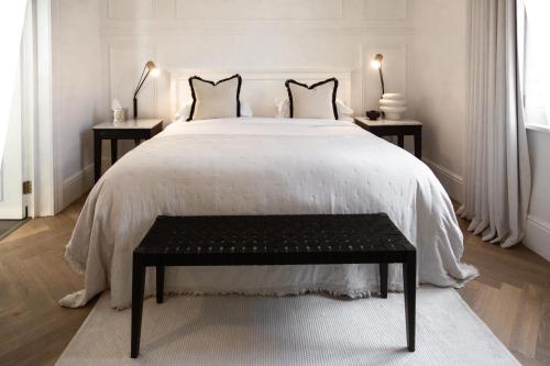开普敦NOAH House的白色卧室设有一张大床和黑色长凳