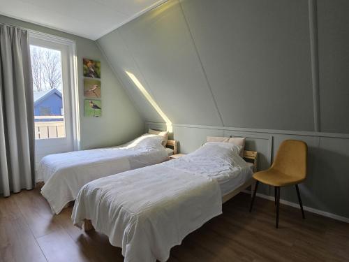 HoogersmildeNatuurvilla De Heerlickheyt的一间卧室设有两张床、一把椅子和一个窗户。
