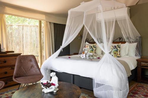 斯库库扎Umkumbe Bush Lodge - Luxury Tented Camp的一间卧室配有一张天蓬床和一把椅子