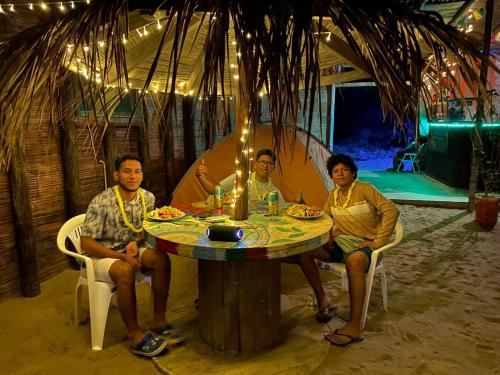 曼克拉Pepon Surf Camp的四人坐在帐篷里,坐在桌子旁