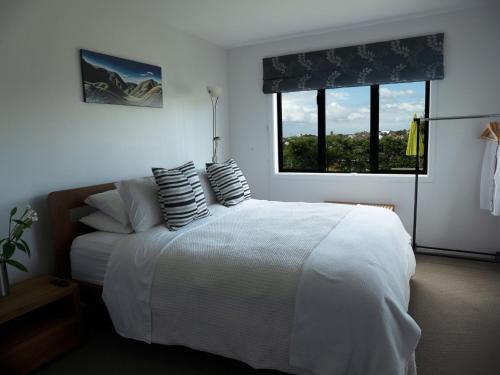 奥克兰Te Rukutai的卧室配有带枕头的白色床和窗户。