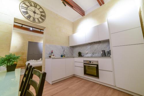 瓦莱塔Valletta Collection - Felix Apartments的厨房配有白色橱柜和墙上的时钟