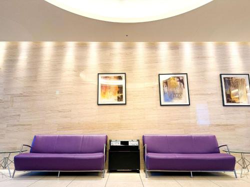 札幌札幌美居酒店的两把紫色椅子放在一个等候室,墙上挂着照片