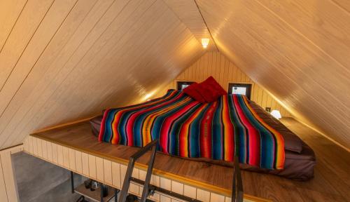 萨拉斯皮尔斯The Sound of Silence - romantic tiny house near Riga的阁楼上一张带彩色条纹棉被的床