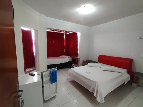 戈亚尼亚Hotel Oliveira的一间卧室配有床和两个带红色窗帘的窗户。