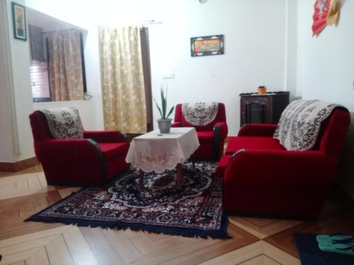 西里古里Areca Holiday Apartment的客厅配有2把红色椅子和桌子