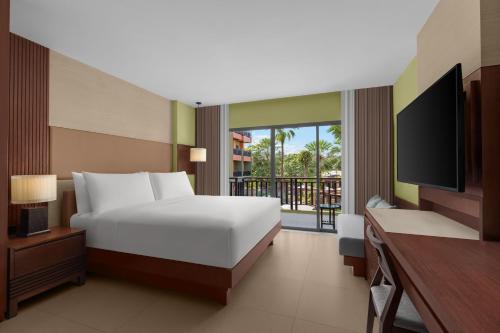芭东海滩Courtyard by Marriott Phuket, Patong Beach Resort的一间卧室设有一张床、一台电视和一个阳台。
