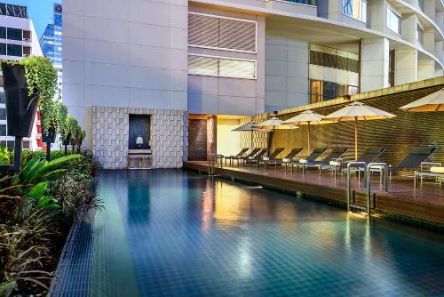 曼谷曼谷阿索克希尔顿酒店 - Hilton Bangkok Grande Asoke的一座带椅子和遮阳伞的大楼前的游泳池