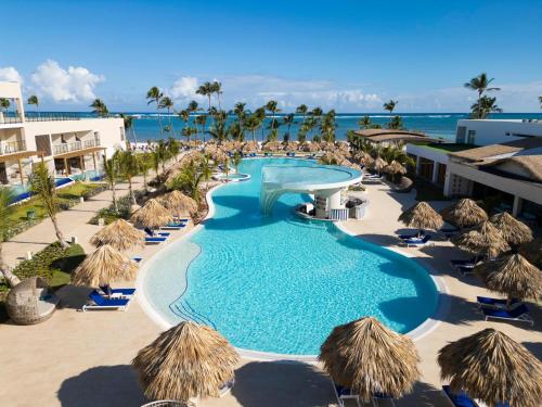 蓬塔卡纳Serenade All Suites - Adults Only Resort的一个带稻草遮阳伞和海洋的游泳池