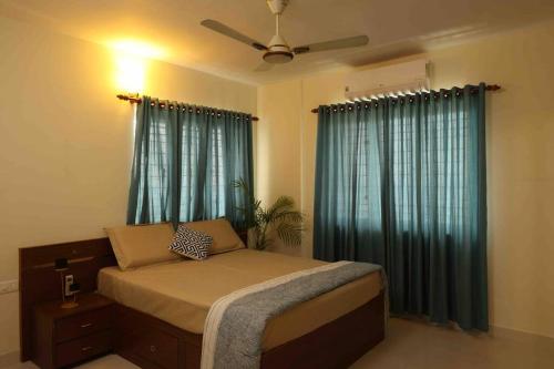 埃尔讷古勒姆Best Serviced Apartments in Cochin Marine drive的一间卧室配有一张带蓝色窗帘的床和风扇