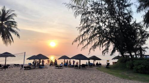 富国FLORA Hotel Phu Quoc的一群人坐在海滩上的伞下