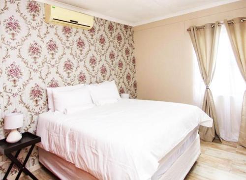 OngwedivaMorningSide Fortyfive的卧室内的一张白色床,配有花卉壁纸