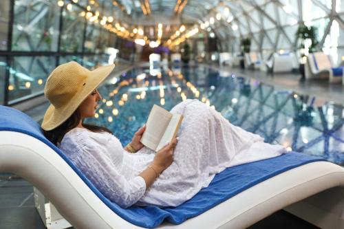多哈羚羊机场酒店 - 仅限转机的坐在椅子上读书的女人在游泳池旁