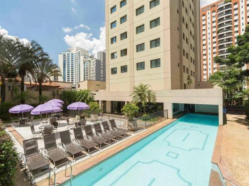 圣保罗Flat Hotel av Macuco São Paulo Ibirapuera UH-2710的大楼前的带椅子和遮阳伞的游泳池