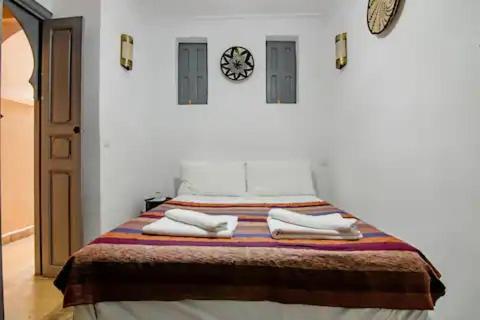 马拉喀什Riad Azawan的一间卧室配有一张带毛巾的床和墙上的时钟