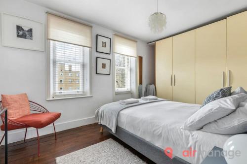 伦敦West Kensington 2Bed Flat的一间卧室配有一张床和一把椅子,还有两个窗户