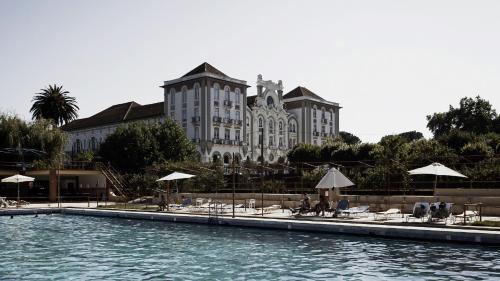 库里亚Curia Palace Hotel & Spa的大楼前的游泳池配有椅子和遮阳伞