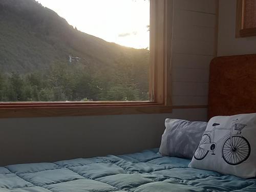 乌斯怀亚LA CABAÑA DEL CAMPO的一张带枕头的床,旁边是窗户,上面有一辆自行车
