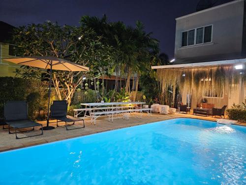 合艾My Home Pool Villa Hatyai的夜间游泳池,配有桌子和遮阳伞