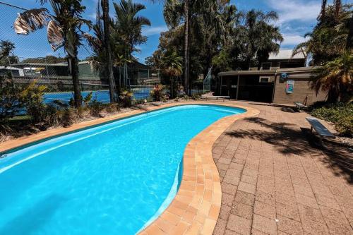 尼尔森湾Leafy seaside unit with lagoon style pool and tennis court的蓝色的游泳池,四周有砖砌的走道