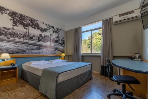 CaçadorBrivali Hotel Centro的配有一张床和一张书桌的酒店客房