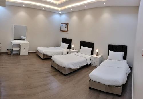 塔伊夫فلل الكناري الراقية的配有白色墙壁和木地板的客房内的三张床