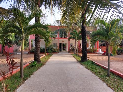 Boukot OuolofLa maison Yaka的棕榈树粉红色建筑前的走道