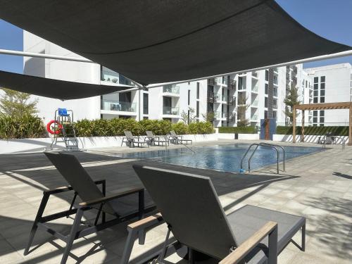 沙迦Modern Sanctuary W/ Pool & Gym access的一个带椅子的庭院和一个带黑伞的游泳池