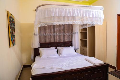 WakisoCrown Inn Bulindo的卧室配有带白色床单和枕头的天蓬床。