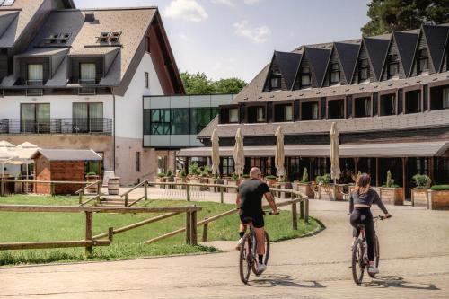 马里博尔Hotel Arena Maribor的一名男子和女子骑着自行车在建筑物前骑行