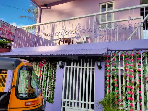 纳苏格布Purple Guesthouse的停在鲜花房子前面的黄色巴士