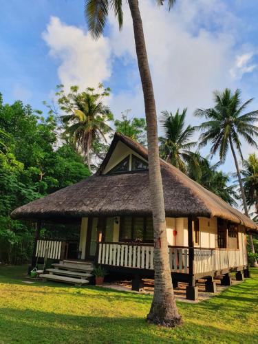 ManiwayaIslas Moriones Beach Resort的茅草屋顶和棕榈树的房子