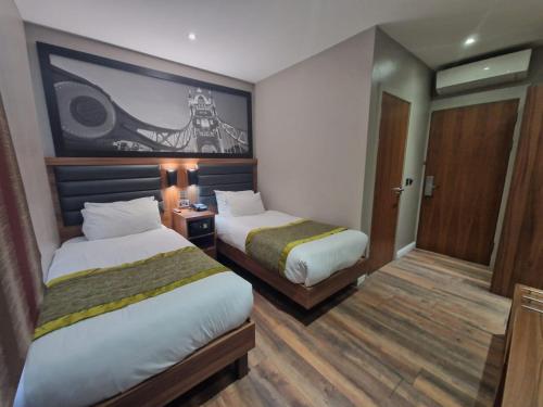 伦敦London Court Hotel的酒店客房设有两张床,墙上挂有绘画作品