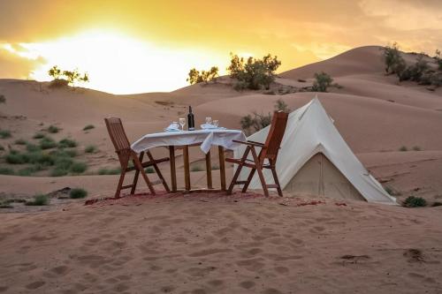 MhamidMhamid Luxury Camp的沙漠中的一张桌子和两把椅子和一个帐篷