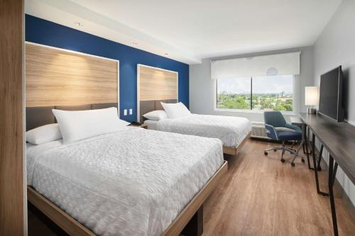 达尼亚滩Tru By Hilton Ft Lauderdale Airport的酒店客房设有两张床、一张书桌和一个窗户。