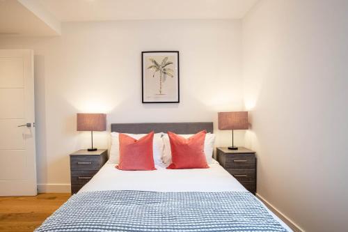 斯劳Deluxe Chic 1 2 Bed Apts near Heathrow Legoland Windsor Slough的一间卧室配有一张带红色枕头的床和两盏灯。