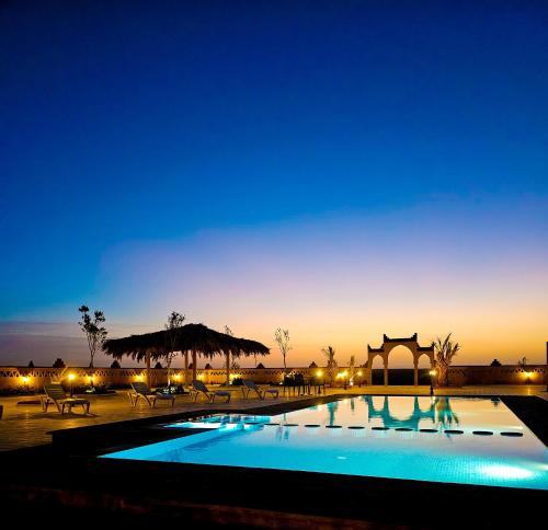 梅尔祖卡Berber Palace Merzouga的夜间带桌椅的游泳池